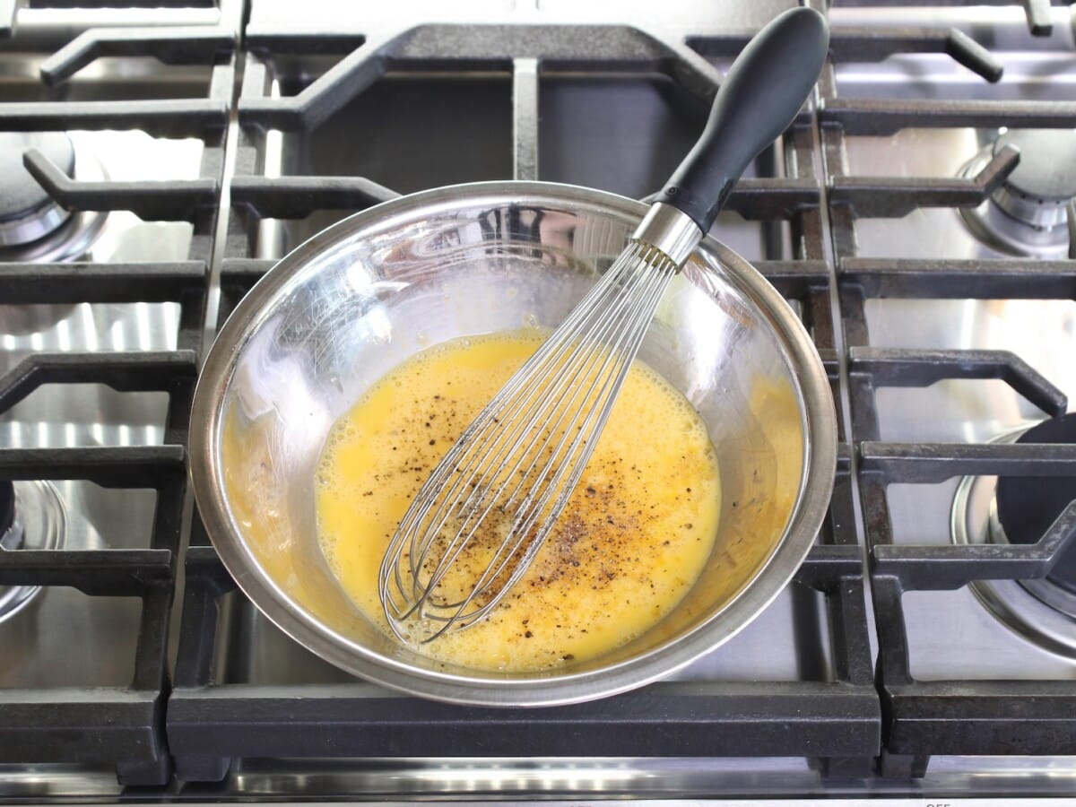 Seasoned beaten egg in a medium mixing bowl with a whisk over the top of cooking range.