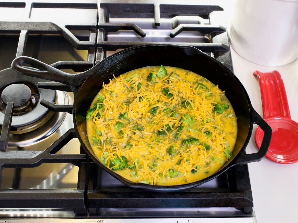 An egg mixture in a large skillet over the top of cooking range. A red teaspoon on the side, and canister in background.