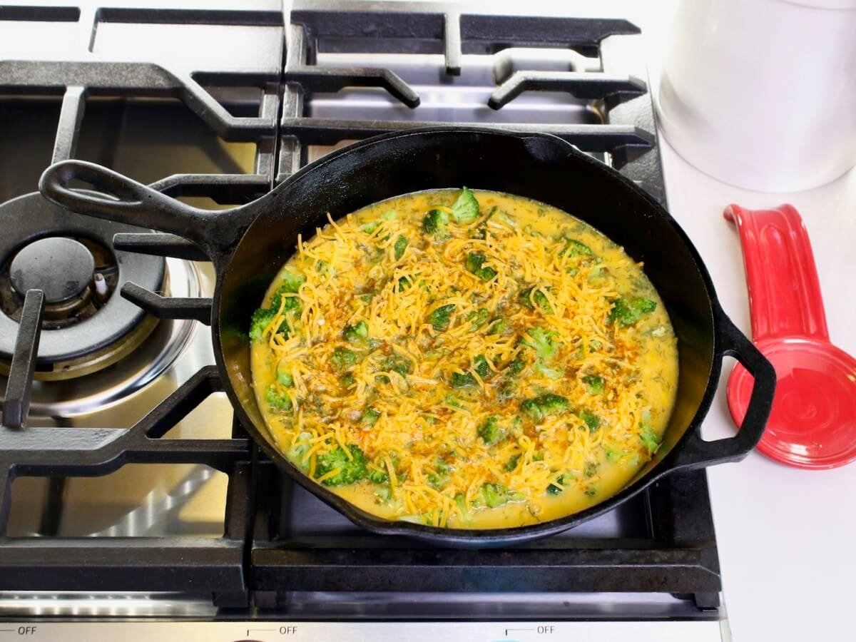 An egg mixture in a large skillet over the top of cooking range. A red teaspoon on the side, and canister in background.