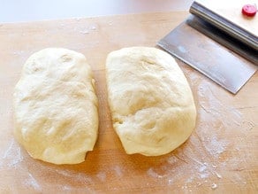 Ball of dough divided in half on a cutting board.