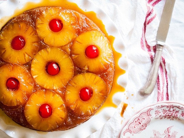 Horizontal image of pineapple upside-down cake on a white plate, accompanied by a knife on the side.