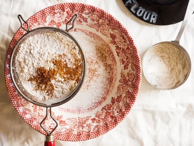 Sifting flour and other dry ingredients into a mixing bowl.