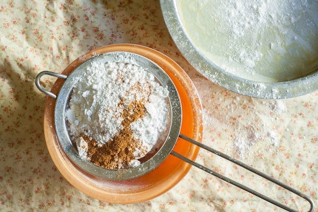 Sifting dry cake ingredients in a metal strainer.