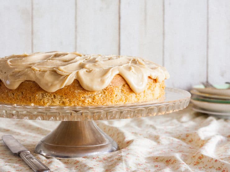 Cider Cake with Caramel Frosting served on a cake holder stand with bright background and a knife on the side