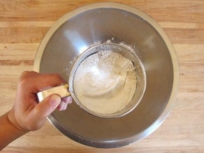 Sifting flour over a mixing bowl.