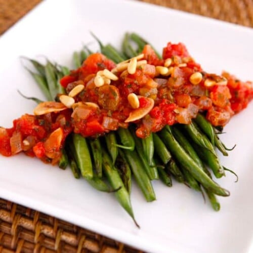 Fresh green beans cooked in a flavorful caponata sauce with tomatoes, onions, and herbs served on a white plate