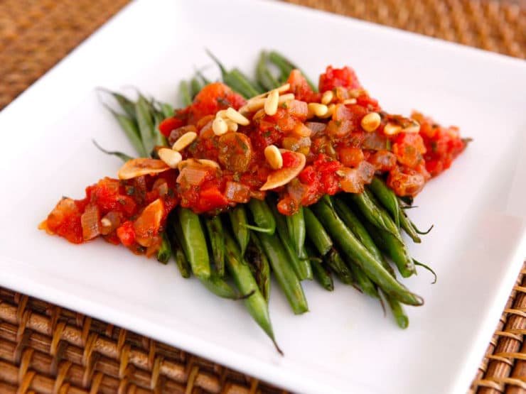 Fresh green beans cooked in a flavorful caponata sauce with tomatoes, onions, and herbs served on a white plate