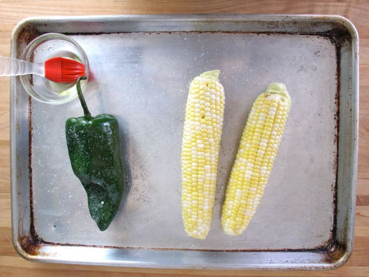 Corn cobs and poblano pepper on a baking sheet.