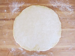 Pizza dough rolled out on a cutting board.