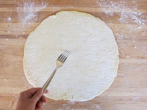Using a fork to poke holes in a pizza crust.