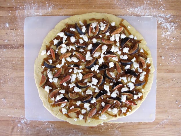Raw pizza crust topped with caramelized onions and figs.