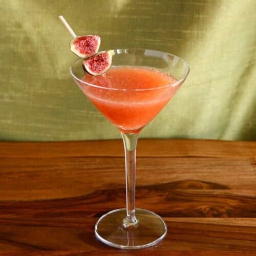 Fig and Honey Cocktail served on a triangle shaped wine glass garnished with figs on a toothpick