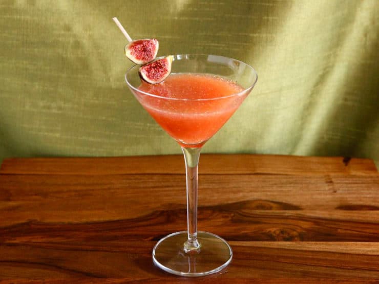 Fig and Honey Cocktail served on a triangle shaped wine glass garnished with figs on a toothpick