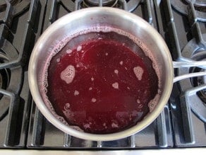 Strained raspberry juice boiling in a small pot.