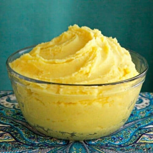 A bowl of saffron mashed potatoes, with a vibrant yellow butter, placed on a table