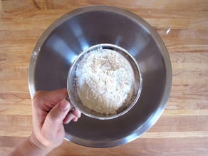 Sifting flour and dry ingredients into a mixing bowl.