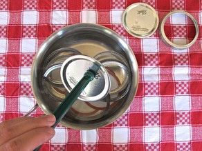 Using tongs to remove sterile lids from simmer water, red checked towel in background.