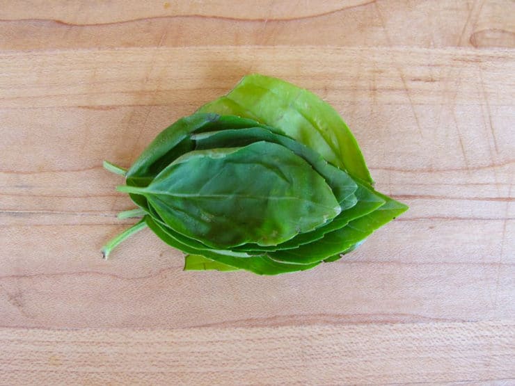 Stack of basil leaves on a cutting board.