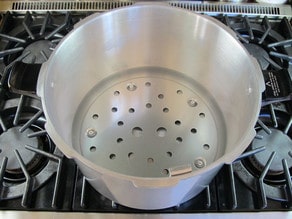 Canning rack inserted into pressure canner without lid on stovetop.