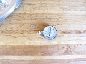 Dial gauge with compression gasket on wooden cutting board.