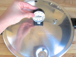 Hand inserting dial gauge into hole in pressure canner lid.