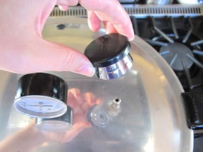 Air vent lock lifted on lid of pressure canner on stovetop.