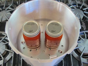 Two jars on canning rack in canner on stovetop.