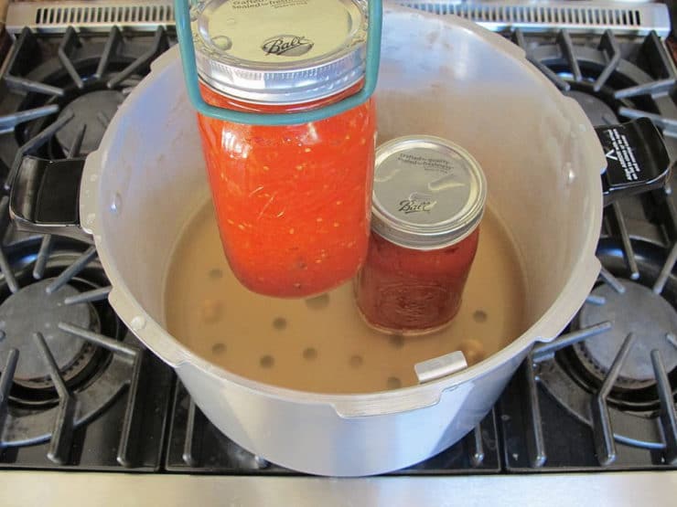 Jar lifter removing jar of tomato sauce from canner with water.