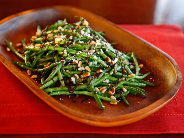 Green Beans with Balsamic Date Reduction, Feta and Pine Nuts served on a wooden plate with a red table clothe