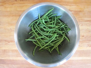 Green beans in a large mixing bowl tossed with oil and seasonings.