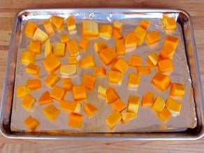 Cubed butternut squash on a lined baking sheet.