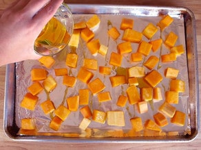 Drizzling oil over cubed butternut squash.