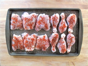 Chicken pieces sprinkled with Seasoning on a baking sheet.
