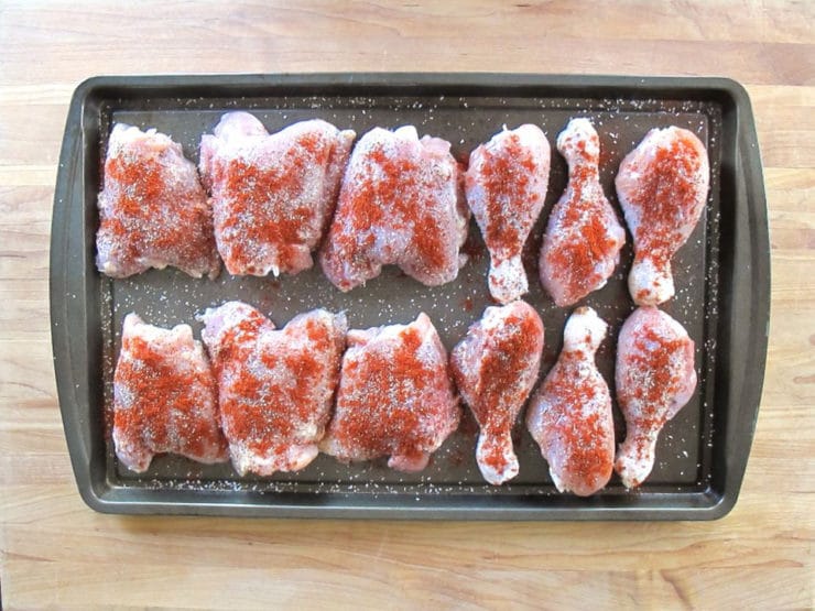Chicken pieces sprinkled with Seasoning on a baking sheet.