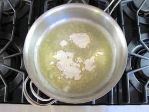 Adding flour to make a roux in a saucepan.