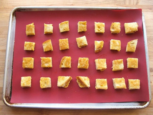 Cubed grilled cheese on a lined baking sheet.