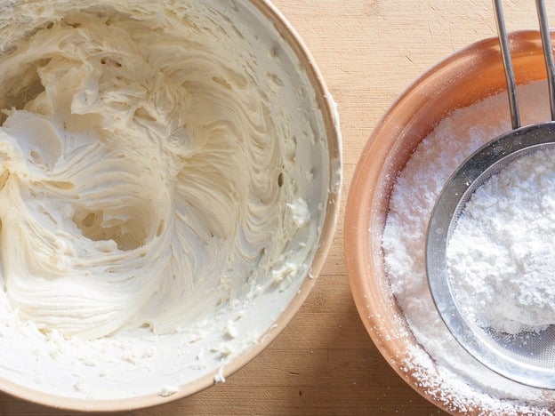 Gradually adding sugar to cream cheese frosting.