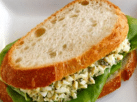 A lightened up egg salad sandwich with lettuce on a white plate.
