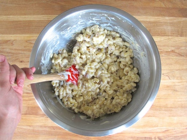 Stirring cheese sauce into cooked noodles.