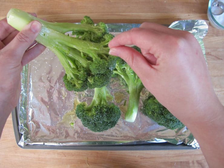 Adding oil and salt on broccoli florets on a lined sheet pan.