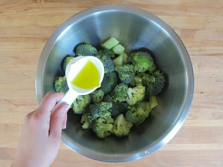 Adding oil to broccoli florets in a mixing bowl.