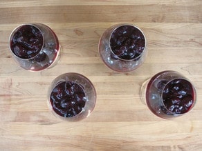 Adding cherry filling on top of cheesecake in glasses.