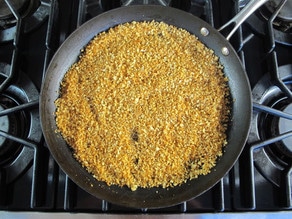 Toasted panko breadcrumbs and red chili pepper flakes in black skillet on stovetop.