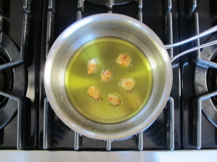 Garlic cloves roasted tender in olive oil in pan on stovetop.
