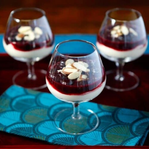 Three glasses of Cherry Cheesecake Shooters topped with almonds and berries, a delightful dessert