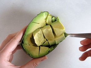 Scooping diced avocado out of the peel with a spoon.