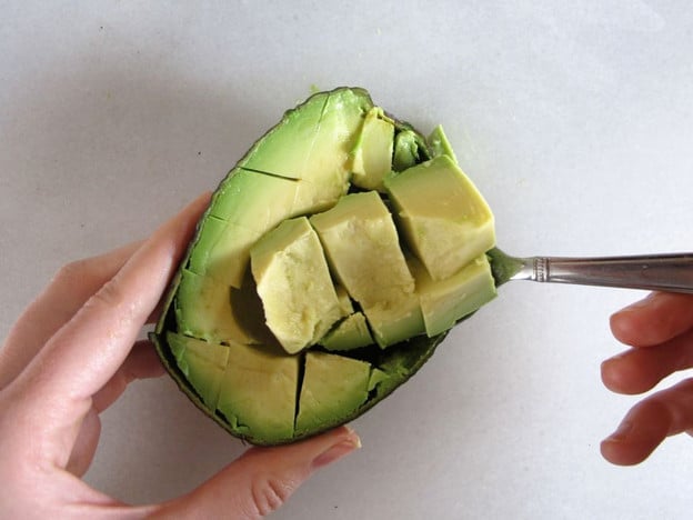 Scooping diced avocado out of the peel with a spoon.