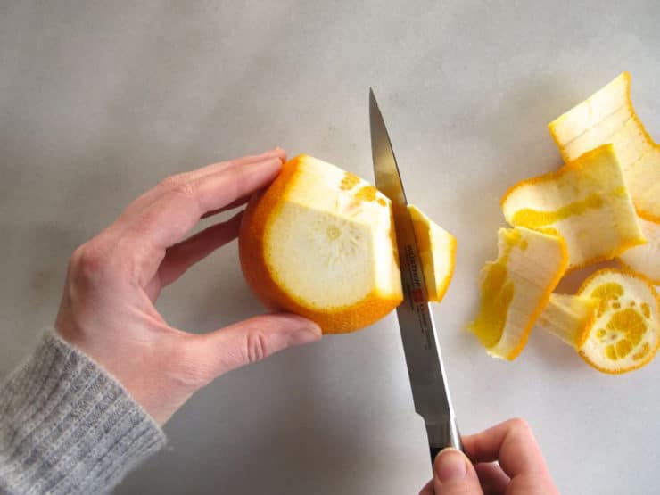 Continuing to remove peel from an orange.