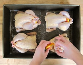 Seasoning Cornish hens in a roasting pan.