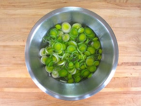 Sliced leeks submerged in a bowl of water.